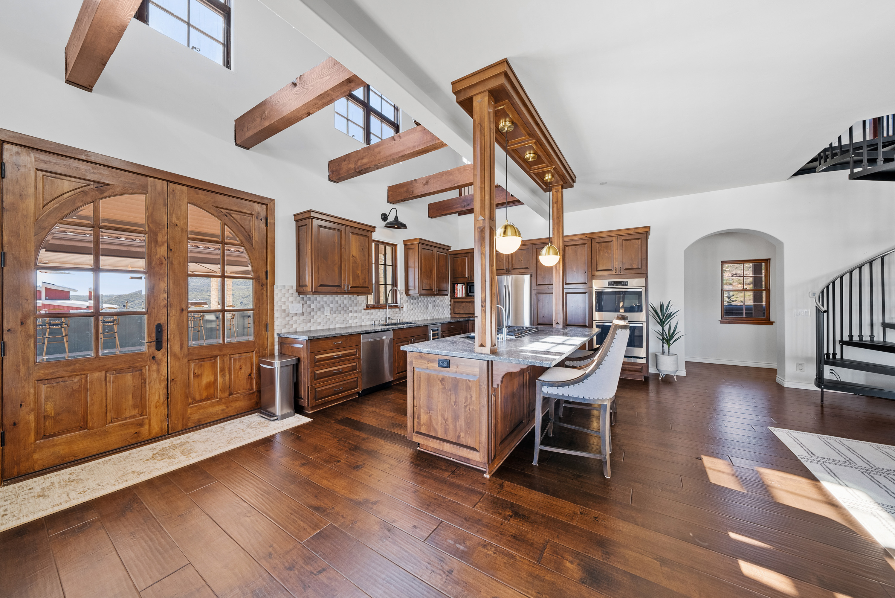 Great room with exposed timber trusses, fireplace, and pool views